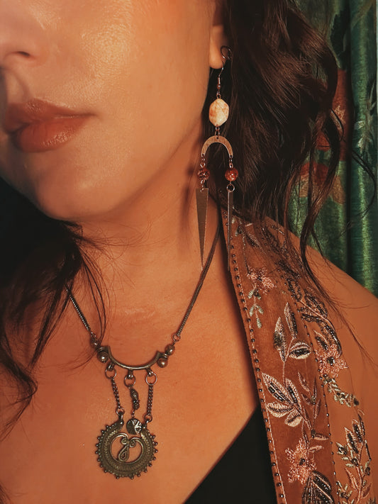 Close-up of a person wearing a detailed necklace and earrings with a patterned garment.