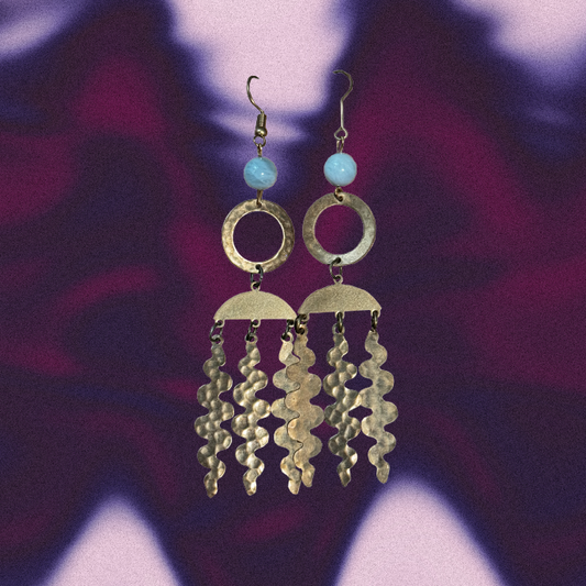 Gold chandelier earrings with blue beads on a colorful abstract background