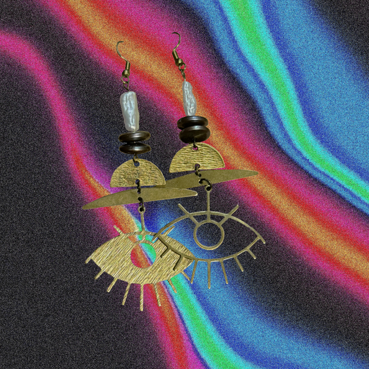 Gold earrings with eye design on a colorful abstract background